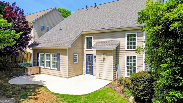 rear view of property featuring fence, a patio area, and a shingled roof