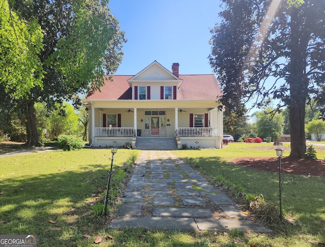 view of front of home with a ceiling fan, a chimney, a front yard, and covered porch