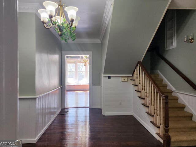 entrance foyer with wood finished floors, ornamental molding, wainscoting, a chandelier, and stairs