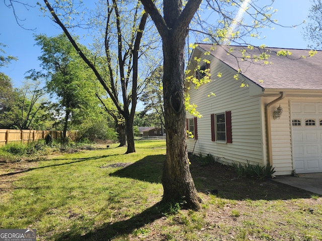 view of side of property featuring an attached garage, fence, a yard, and roof with shingles