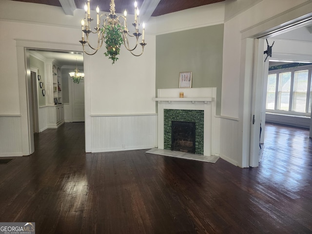 unfurnished living room with a tile fireplace, an inviting chandelier, wainscoting, and dark wood-type flooring