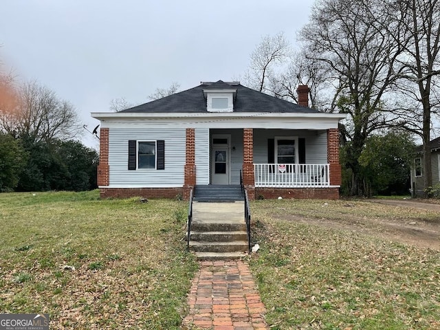 bungalow-style home featuring a front yard, covered porch, and a chimney