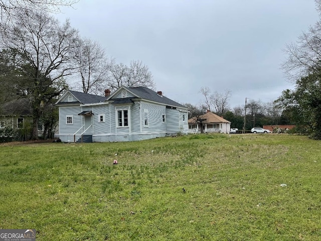 view of property exterior featuring entry steps, a chimney, central AC, and a lawn