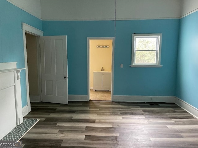 unfurnished bedroom with wood finished floors, ensuite bathroom, a sink, and baseboards