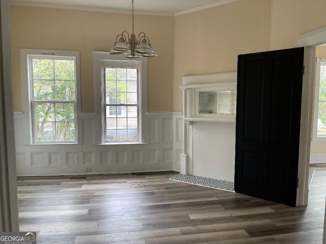 unfurnished dining area with a decorative wall, ornamental molding, a chandelier, wainscoting, and wood finished floors