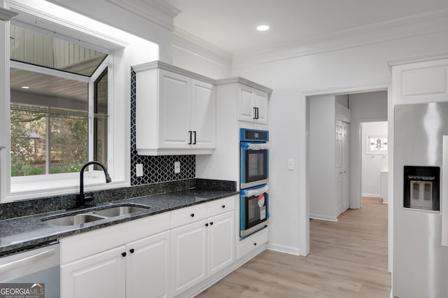 kitchen featuring tasteful backsplash, white cabinetry, stainless steel appliances, light wood finished floors, and a sink