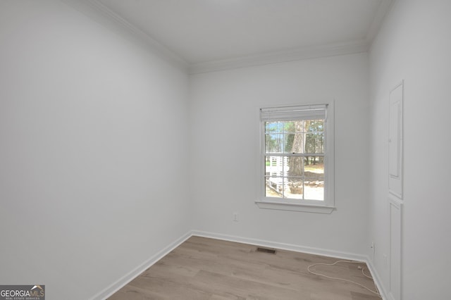 empty room featuring light wood finished floors, visible vents, baseboards, and ornamental molding