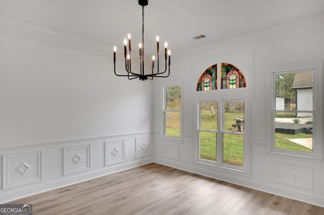 unfurnished dining area with visible vents, a decorative wall, ornamental molding, a chandelier, and light wood-style flooring