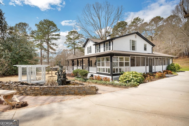 view of home's exterior with a shingled roof, a sunroom, and a chimney