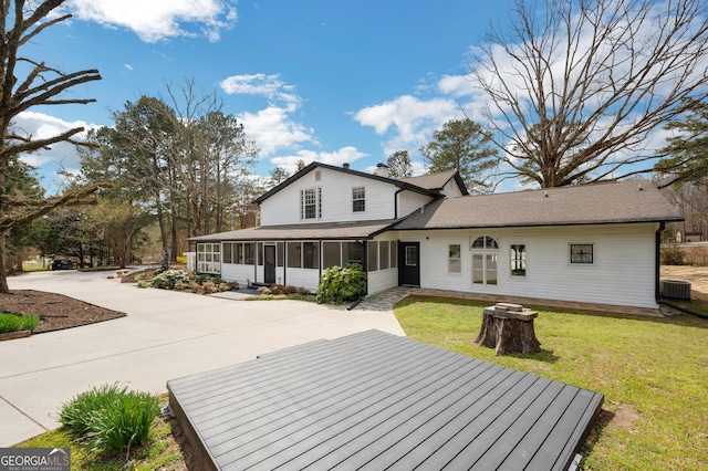 exterior space with a shingled roof, a sunroom, a yard, cooling unit, and concrete driveway