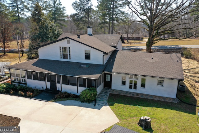 rear view of property with a shingled roof, cooling unit, a sunroom, and a lawn