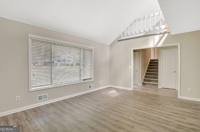 unfurnished living room with visible vents, baseboards, light wood-style floors, stairs, and lofted ceiling