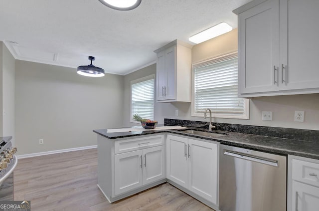 kitchen featuring dark stone countertops, a peninsula, light wood-style flooring, appliances with stainless steel finishes, and a sink