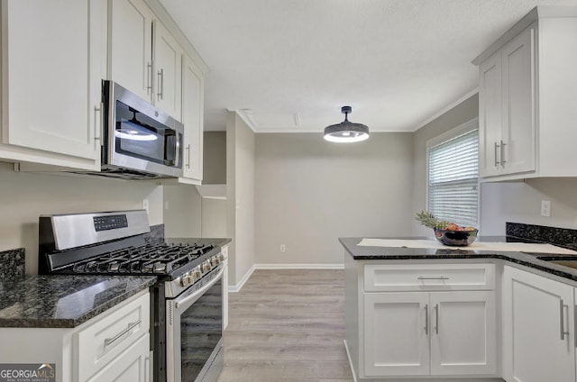 kitchen with a peninsula, light wood-style flooring, white cabinets, dark stone counters, and appliances with stainless steel finishes