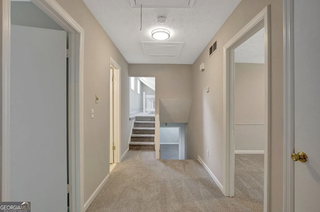 hallway featuring visible vents, a textured ceiling, baseboards, and carpet floors