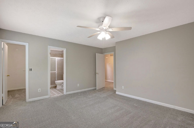 unfurnished bedroom with baseboards, ensuite bath, a ceiling fan, a walk in closet, and carpet