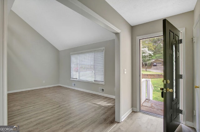 entrance foyer featuring light wood-style flooring, baseboards, vaulted ceiling, and visible vents