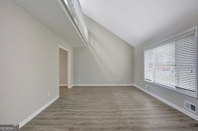 unfurnished living room featuring visible vents, baseboards, wood finished floors, and lofted ceiling