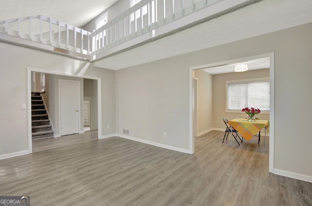 unfurnished living room featuring visible vents, baseboards, a towering ceiling, wood finished floors, and stairs