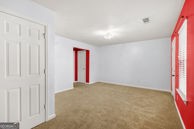 carpeted empty room featuring a healthy amount of sunlight, baseboards, and visible vents