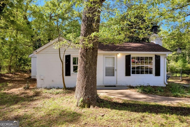 view of front of property with concrete block siding, a chimney, fence, and roof with shingles