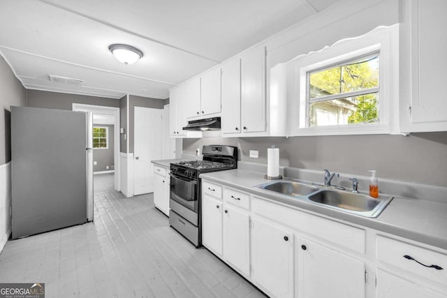 kitchen featuring stainless steel appliances, under cabinet range hood, a sink, and white cabinetry