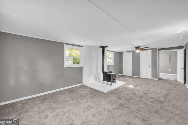 basement featuring a wood stove, carpet, baseboards, and ceiling fan
