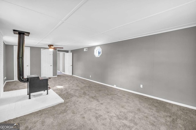 basement featuring carpet flooring, ceiling fan, baseboards, and a wood stove