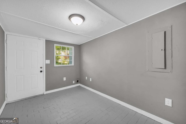 spare room with electric panel, baseboards, and a textured ceiling