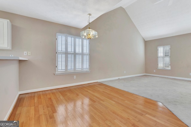 unfurnished dining area featuring a chandelier, light wood-type flooring, baseboards, and lofted ceiling