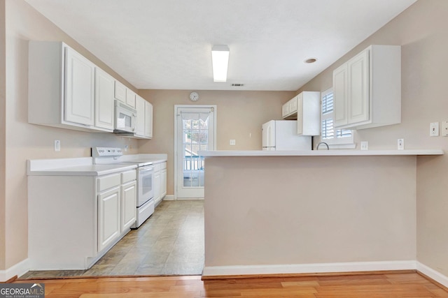 kitchen with white appliances, white cabinetry, light countertops, and a peninsula