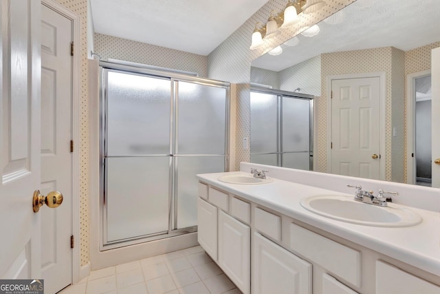 bathroom featuring a sink, a stall shower, and wallpapered walls