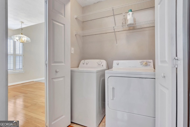 laundry room with laundry area, independent washer and dryer, light wood-type flooring, a chandelier, and baseboards