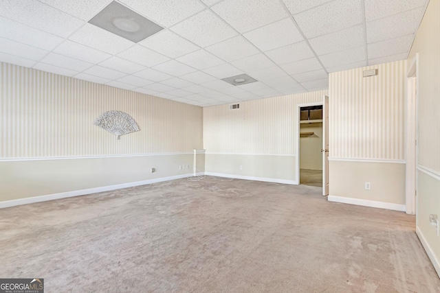 carpeted spare room with visible vents, baseboards, and a drop ceiling