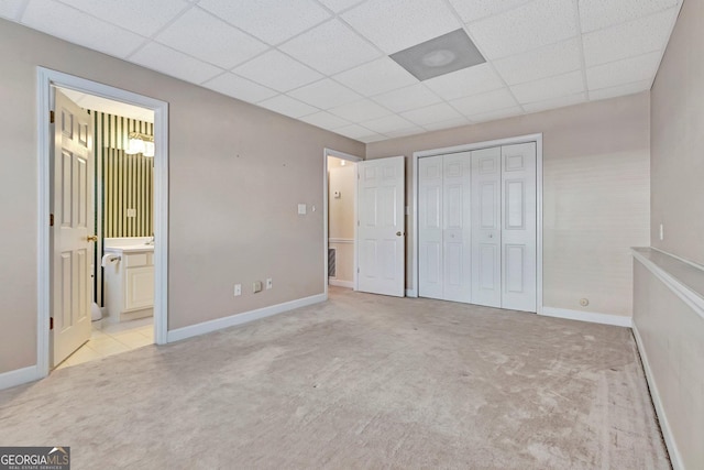 unfurnished bedroom featuring a closet, baseboards, ensuite bathroom, a paneled ceiling, and light carpet