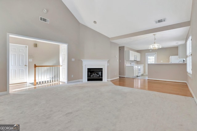 unfurnished living room featuring visible vents, baseboards, a chandelier, high vaulted ceiling, and light carpet
