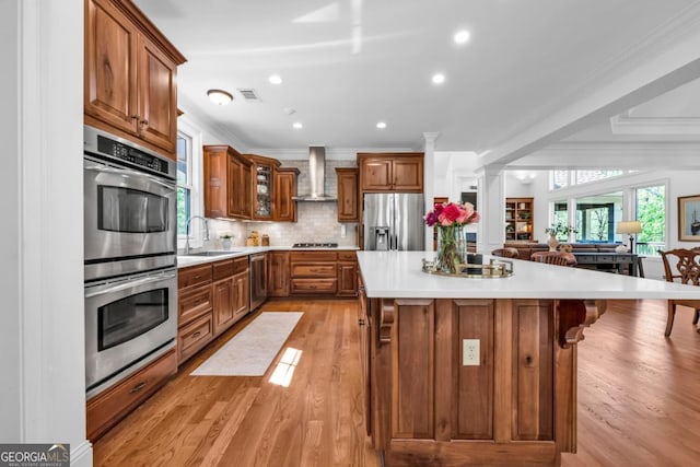 1021 Homestead, Greensboro, GA 30642 - kitchen with stainless steel appliances, a sink, wall chimney exhaust hood, brown cabinetry, and ornamental molding