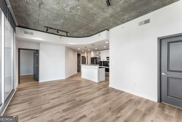 unfurnished living room featuring light wood-type flooring, baseboards, track lighting, and visible vents