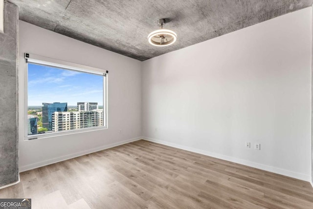empty room with a view of city, baseboards, and wood finished floors