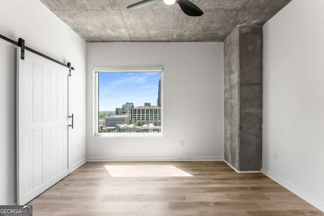 unfurnished bedroom with baseboards, wood finished floors, ceiling fan, and a barn door