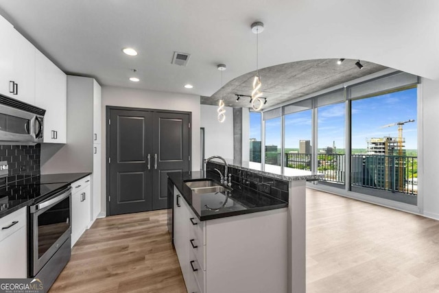kitchen featuring light wood finished floors, a sink, tasteful backsplash, visible vents, and appliances with stainless steel finishes