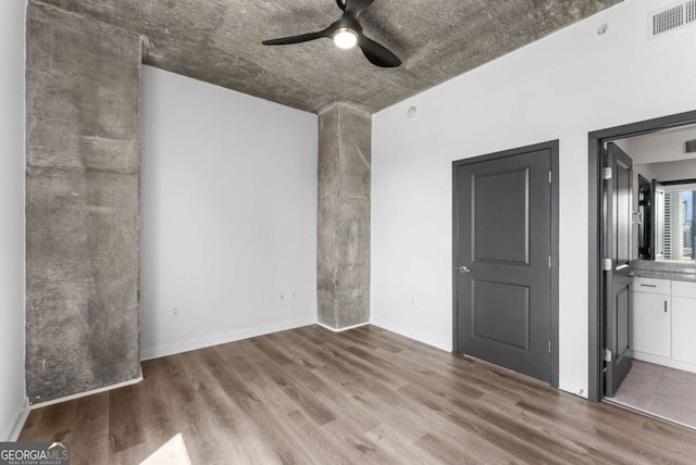 unfurnished bedroom with connected bathroom, a ceiling fan, wood finished floors, and visible vents