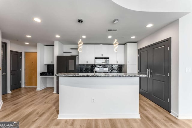 kitchen with tasteful backsplash, light wood-style flooring, white cabinetry, decorative light fixtures, and stainless steel appliances