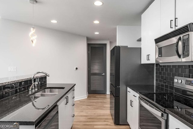 kitchen featuring light wood finished floors, stainless steel appliances, white cabinets, a sink, and decorative backsplash