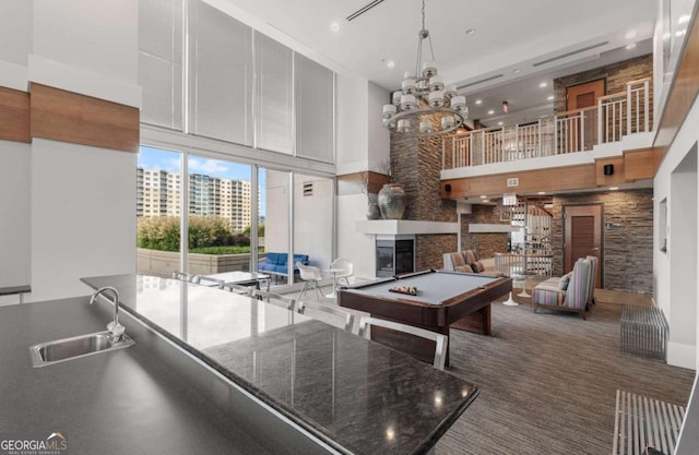 recreation room with a notable chandelier, a high ceiling, a sink, recessed lighting, and a glass covered fireplace