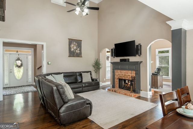 living area with dark wood-style flooring, a fireplace, a high ceiling, ceiling fan, and arched walkways