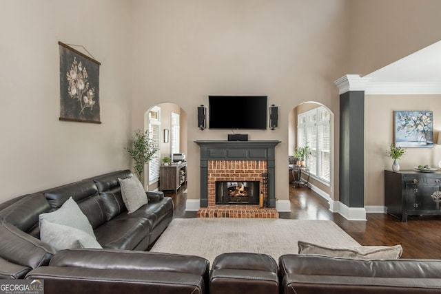 living room with arched walkways, a brick fireplace, baseboards, and wood finished floors
