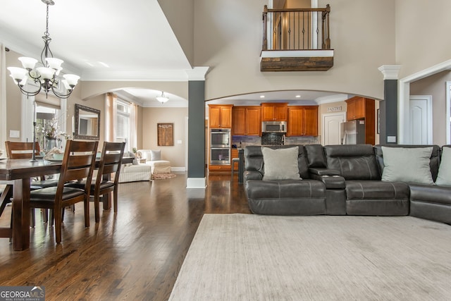 living room with ornamental molding, arched walkways, a notable chandelier, and dark wood-style floors
