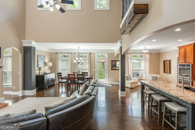 living room featuring arched walkways, a high ceiling, ceiling fan with notable chandelier, and dark wood finished floors