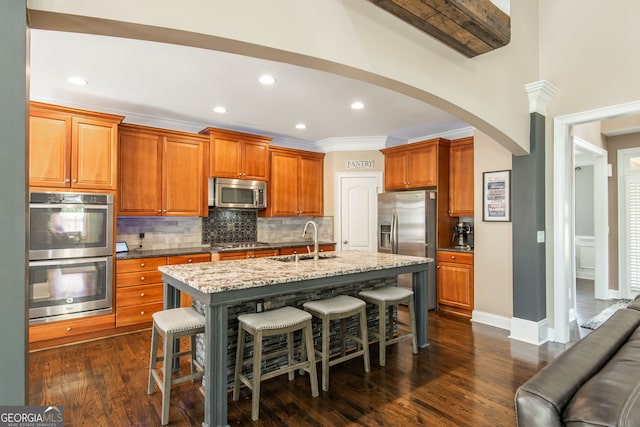 kitchen featuring backsplash, a breakfast bar area, stainless steel appliances, arched walkways, and a sink
